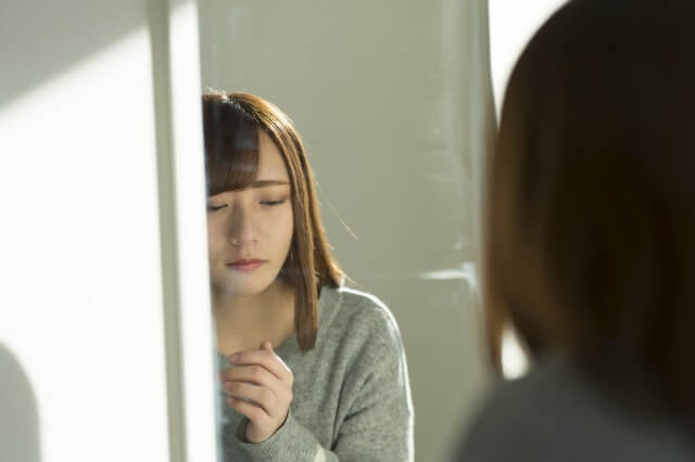 女性が鏡の前でうつむいて悲しい顔をしている様子の画像